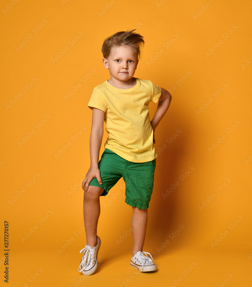 Full length portrait of an excited young boy posing happy smiling in green shorts over yellow Full length portrait of an excited young boy posing happy smiling in green shorts over yellow