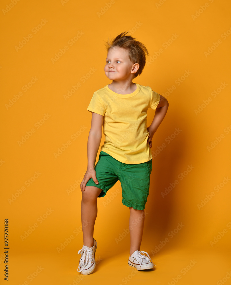 Full length portrait of an excited young boy posing happy smiling in green shorts over yellow Full length portrait of an excited young boy posing happy smiling in green shorts over yellow
