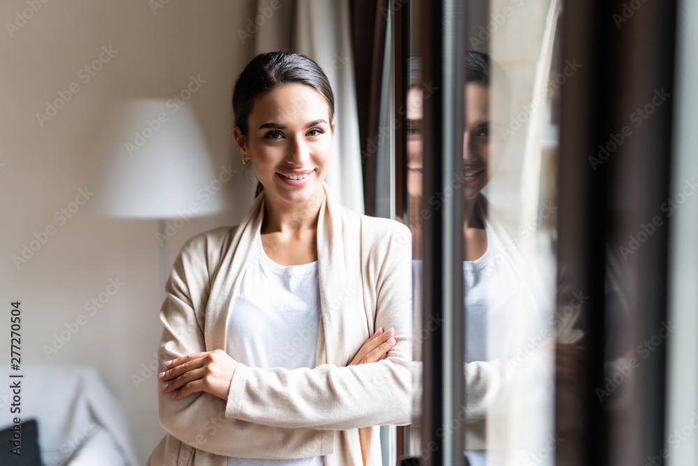 Happy young woman thinking and looking at side beside a window at home Happy young woman thinking and looking at side beside a window at home