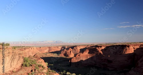 Wide view of the Canyon de Chelly, a sandstone geologic formation and the green vegetation on the rim drive.