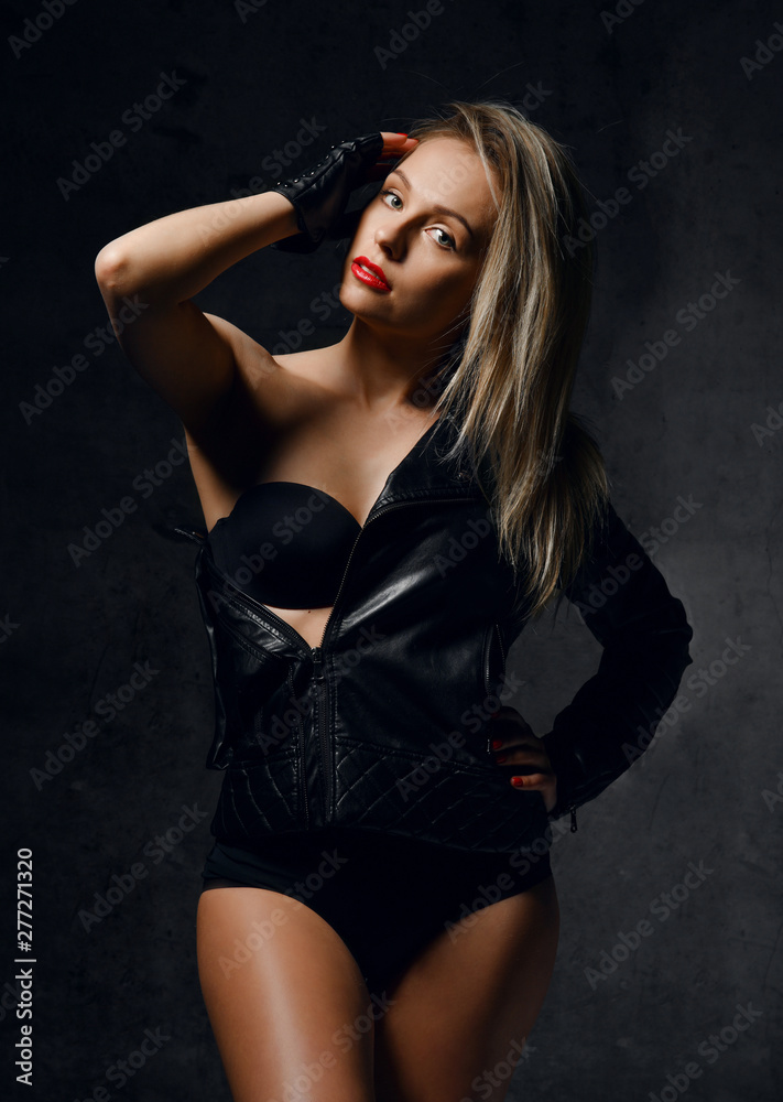 Young sensual beautiful sexy woman posing in fashion black leather jacket on dark wall 