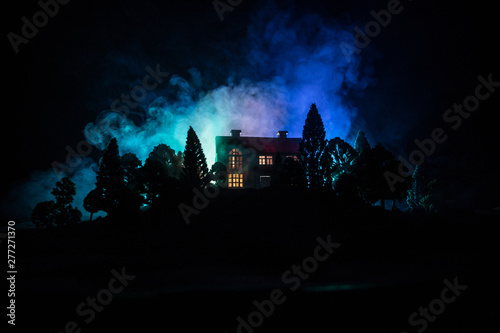Old house with a Ghost in the forest at night or Abandoned Haunted Horror House in fog. Old mystic building in dead tree forest. Trees at night with moon. Surreal lights.