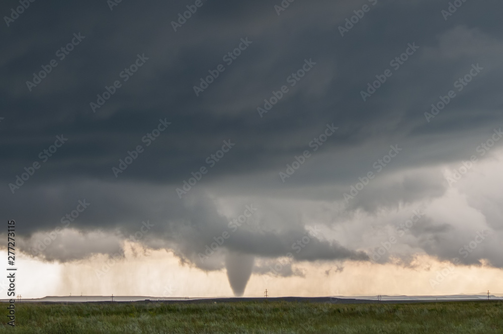 A cone tornado touches down under the base of a dark storm on the plains in Wyoming.