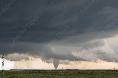 A cone tornado touches down under the base of a dark storm on the plains in Wyoming.