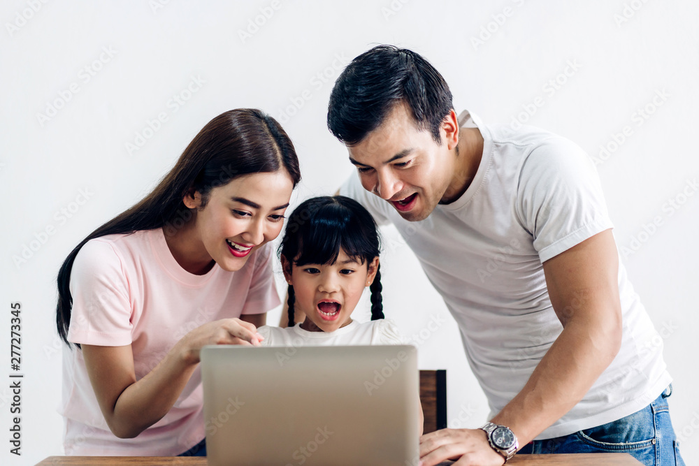 Fototapeta premium Happy family father and mother with daughter sitting and looking at laptop computer together in the living room at home