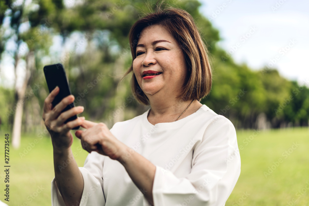 Portrait of happy senior adult elderly asia women smiling and using and talking on the phone in the park.Retirement concept Portrait of happy senior adult elderly asia women smiling and using and talking on the phone in the park.Retirement concept