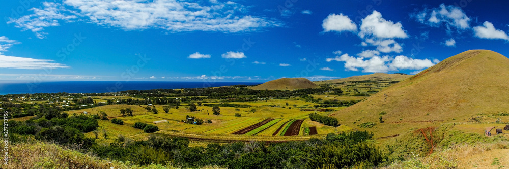 Fototapeta premium Panoramic view of Easter Island from Puna Pau, where the pukao (moai topknots) were carved, showcasing the island's lush landscape under a sunny sky with scattered clouds
