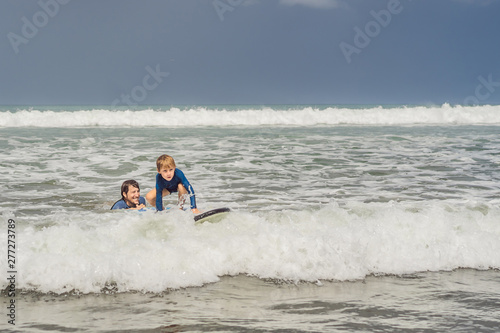 Father or instructor teaching his 5 year old son how to surf in the sea on vacation or holiday. Travel and sports with children concept. Surfing lesson for kids