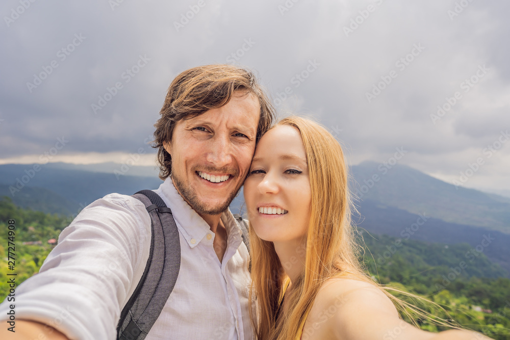 Man and woman making selfie on background of Batur volcano and Agung mountain view at morning from Kintamani, Bali, Indonesia