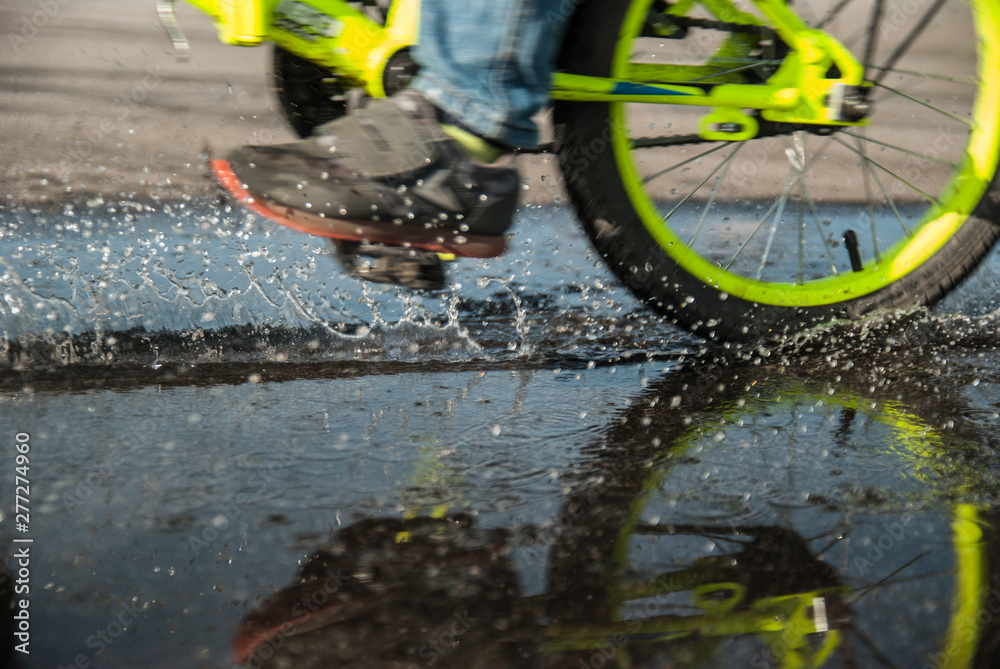 Child crossing the puddle on his bicyc;e, with motion blur and a lot of water drops