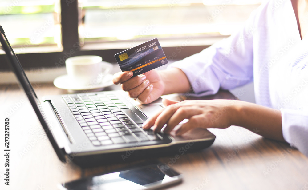 Woman hands holding credit card and using laptop for online shopping in a office table coffee cup background / working people paying technology money wallet online payment at home Woman hands holding credit card and using laptop for online shopping in a office table coffee cup background / working people paying technology money wallet online payment at home