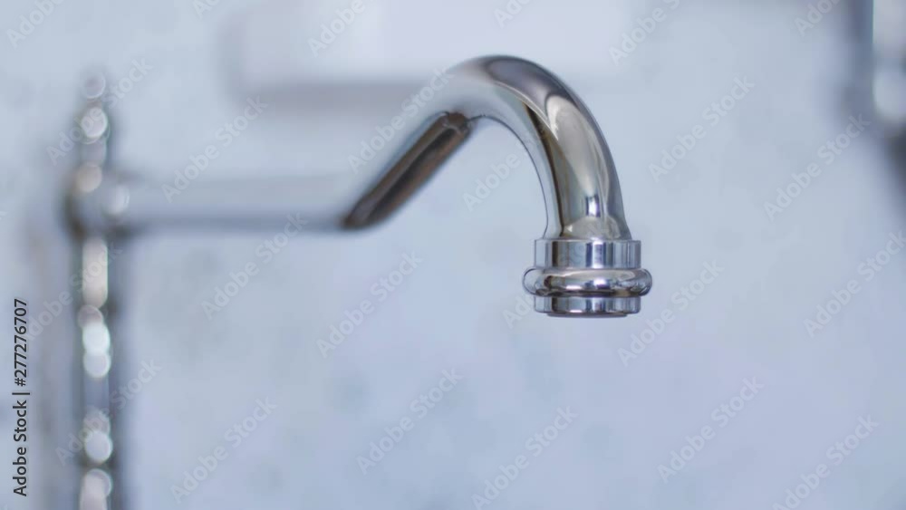 Clean tap water for washing dishes starts flowing from long, cute, new bright, steel and curved tap in light kitchen when someone turned it on in daylight. Clean tap water for washing dishes starts flowing from long, cute, new bright, steel and curved tap in light kitchen when someone turned it on in daylight.