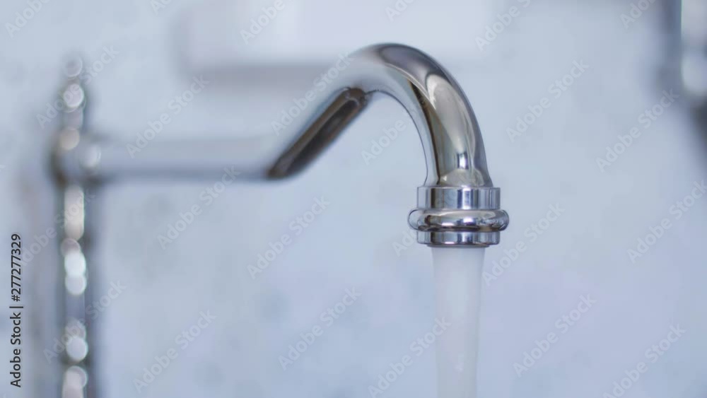 Closeup view of clean tap water for washing dishes starts flowing from long, cute, new bright, steel, curved tap in light kitchen when someone turned it on in daylight. Closeup view of clean tap water for washing dishes starts flowing from long, cute, new bright, steel, curved tap in light kitchen when someone turned it on in daylight.
