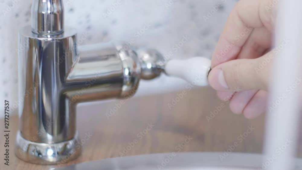 Someone's hand is touching and moving clean tap water faucet so water could start flowing from long, cute, new bright, steel tap in light kitchen when someone turned it on in daylight. Someone's hand is touching and moving clean tap water faucet so water could start flowing from long, cute, new bright, steel tap in light kitchen when someone turned it on in daylight.
