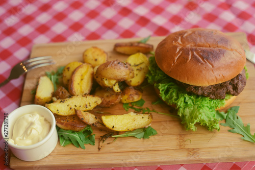 Meat burger with fries, mayonnaise potatoes on a wooden board. Restaurant dish. Food in the cafe, eatery. Fast food. A fat dish. burger with meat and lettuce. Board on the tablecloth in the cell photo