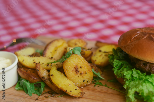 Meat burger with fries, mayonnaise potatoes on a wooden board. Restaurant dish. Food in the cafe, eatery. Fast food. A fat dish. burger with meat and lettuce. Board on the tablecloth in the cell photo