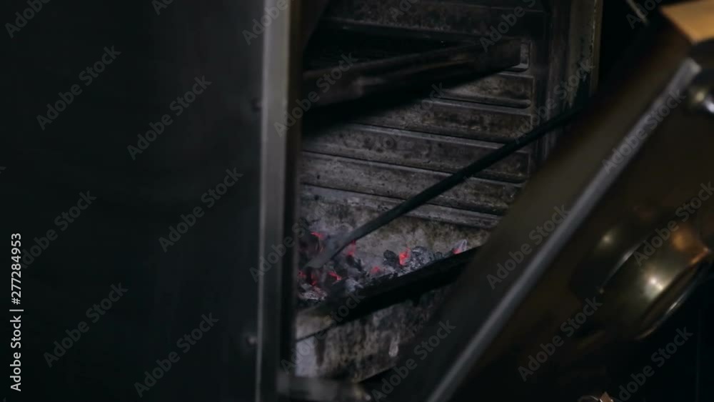 Close-up of a man mixing coals in a professional barbecue stove. Cooking meat or fish on the grill in the restaurant. Close-up of a man mixing coals in a professional barbecue stove. Cooking meat or fish on the grill in the restaurant.