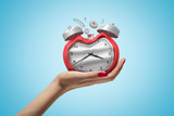 Side closeup of woman's hand facing up and holding damaged retro alarm clock on light blue gradient background.