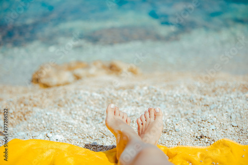 woman legs on yellow blanket at sunny beach close up