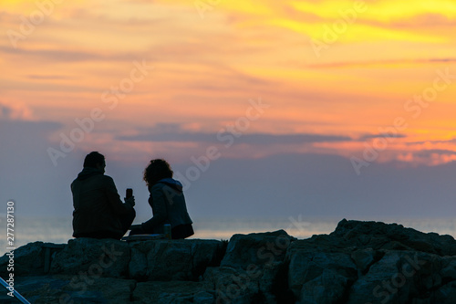 couple sitting on rocky cliff looking on sunset. romantic date