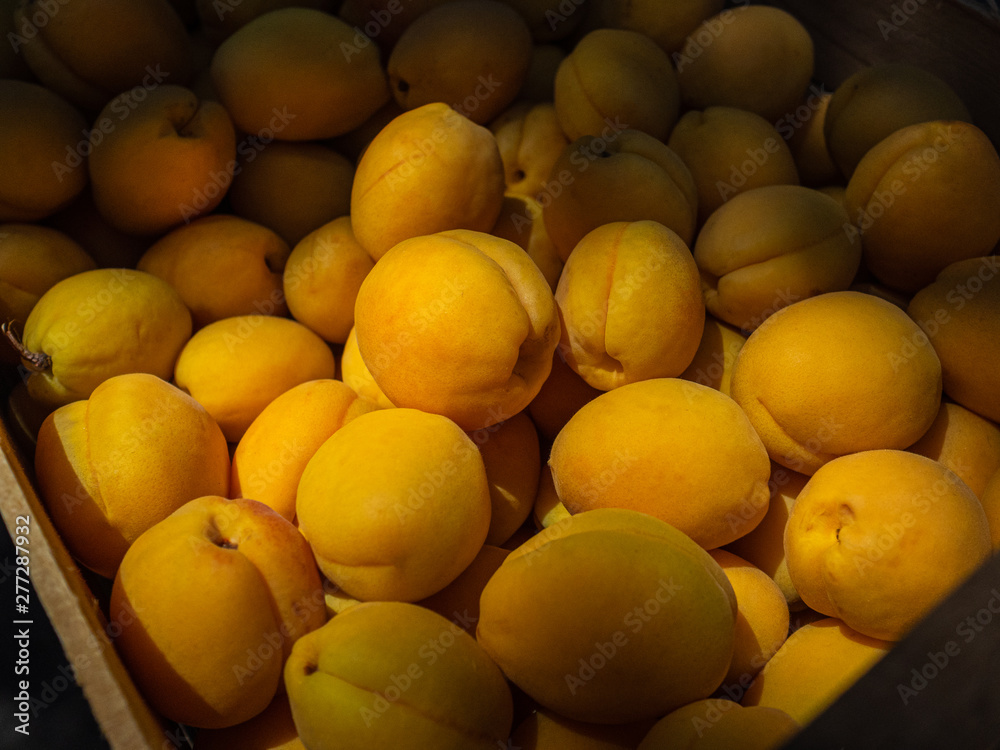 Ripe, sweet apricots in a wooden box on the market. The sun lights the apricots on the market Ripe, sweet apricots in a wooden box on the market. The sun lights the apricots on the market
