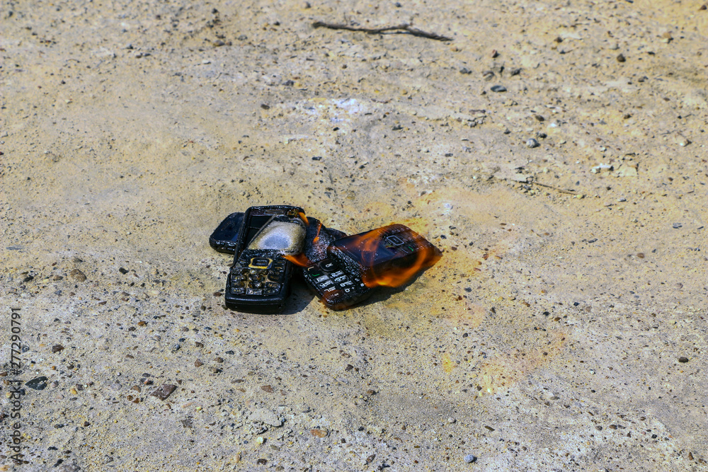burnt mobile phones on textural concrete background. Concept: Danger of using low-quality cell phones.