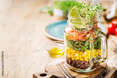 Fresh spring salad with salmon, quinoa, arugula, cress salad and corn in a mason jar for a snack with you. The concept of healthy proper nutrition. photo