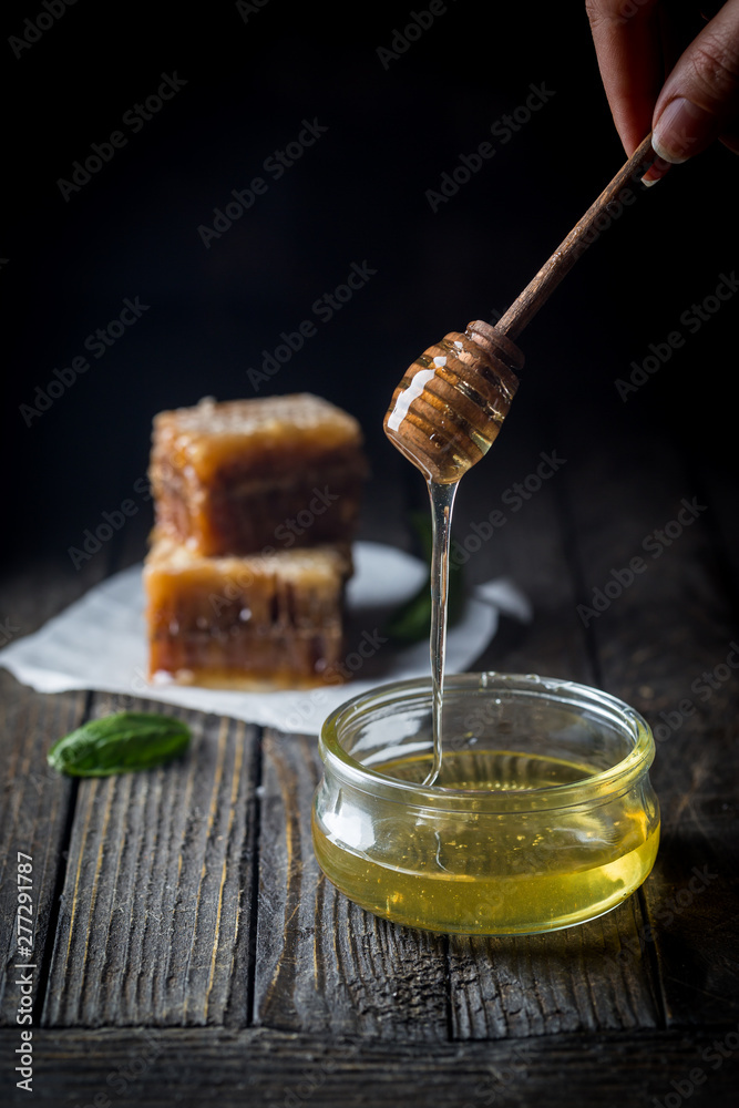 Honey dripping from honey dipper in glass jar with honeycomb over dark background. Honey dripping from honey dipper in glass jar with honeycomb over dark background.