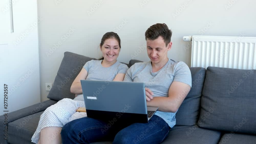 Young couple, man and woman are watching comedy movie on laptop and laughing sitting on sofa. They are in their modern apartment. Young couple, man and woman are watching comedy movie on laptop and laughing sitting on sofa. They are in their modern apartment.