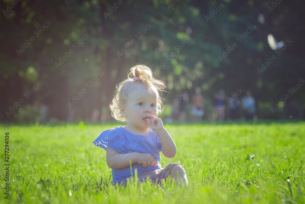 Cute little girl sits on the green grass, outdoors, summer time, blurred background Cute little girl sits on the green grass, outdoors, summer time, blurred background