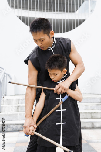 Father and son are engaged in Wushu in the city. The photo illustrates a healthy lifestyle and sport. The father trains the son.
