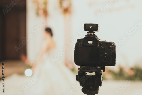 Close-up of professional DSLR digitak camera attached with tripod in wedding ceremony and with bride in wedding dress blurred out in background photo