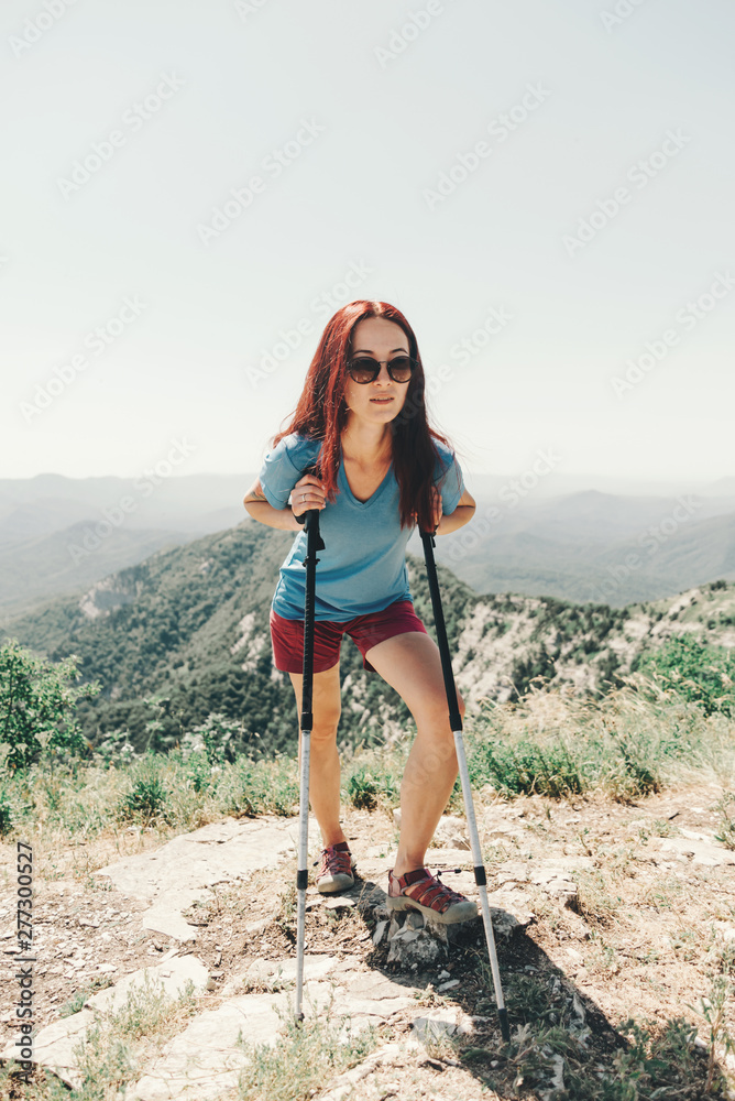 Sporty woman standing and resting with trekking poles in mountains.
