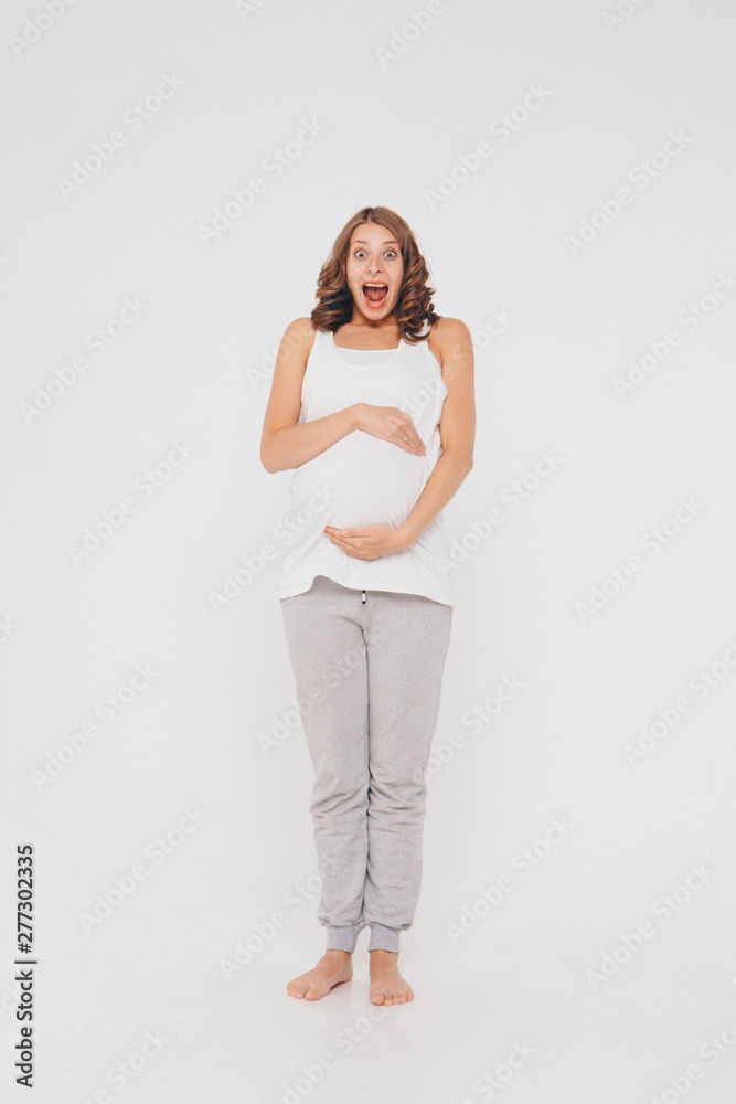 pregnant woman in sportswear on white background. The girl holds her stomach with her mouth wide open and a surprised expression on her face pregnant woman in sportswear on white background. The girl holds her stomach with her mouth wide open and a surprised expression on her face