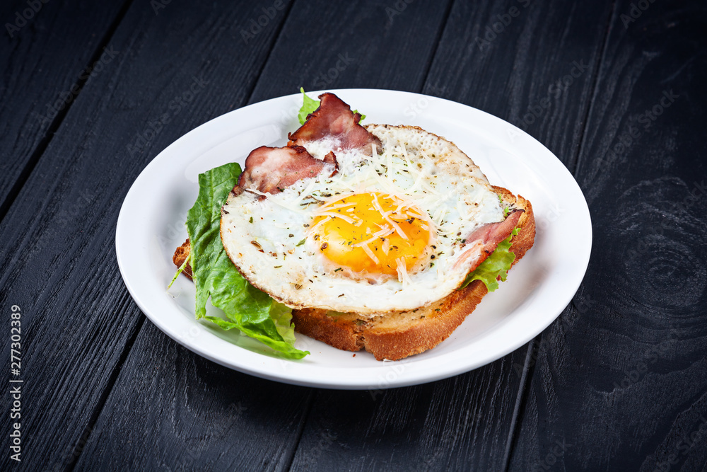 Close up view on toast with fried egg, bacon melted cheese and lettuce. Breakfast food. Fried toast on dark background. Snack. Copy space