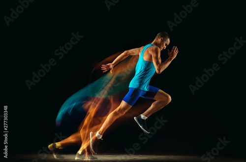 Fotografie, Obraz Professional male runner training isolated on black studio background in mixed light