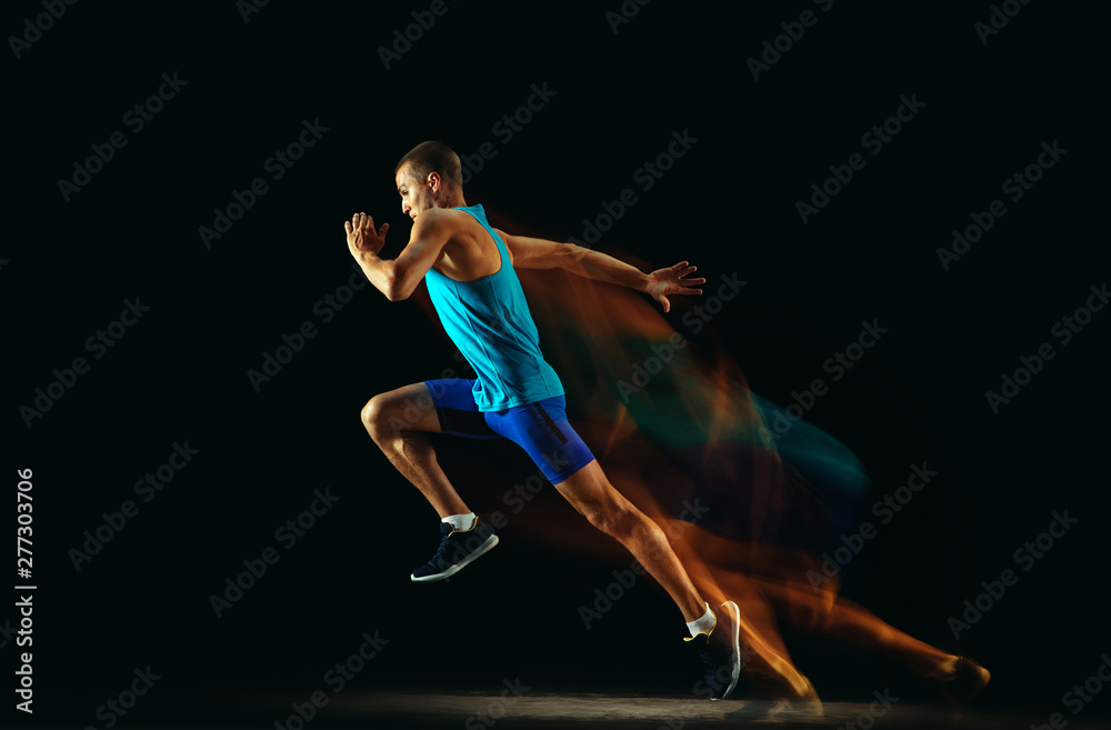 Professional male runner training isolated on black studio background in mixed light. Man in sportsuit practicing in run or jogging. Healthy lifestyle, sport, workout, motion and action concept.