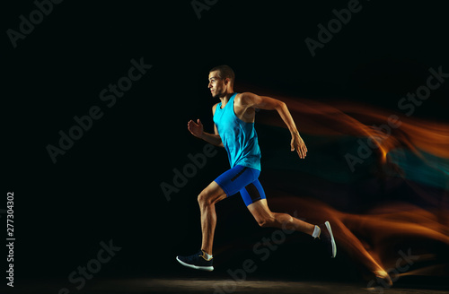 Professional male runner training isolated on black studio background in mixed light. Man in sportsuit practicing in run or jogging. Healthy lifestyle, sport, workout, motion and action concept. © master1305