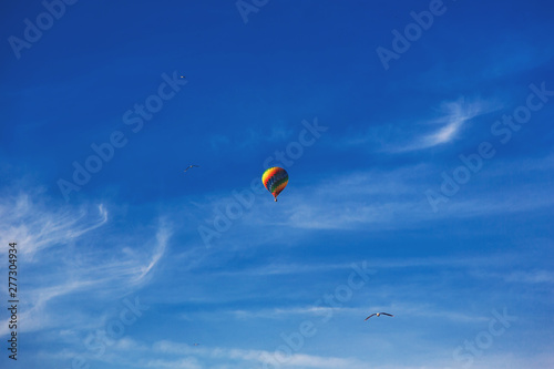 Balloon flying through the blue sky among the clouds. Freedom, adventure, loneliness. Birds are stolen around