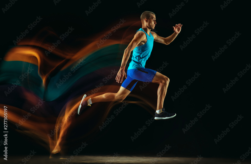 Professional male runner training isolated on black studio background in mixed light. Man in sportsuit practicing in run or jogging. Healthy lifestyle, sport, workout, motion and action concept. Professional male runner training isolated on black studio background in mixed light. Man in sportsuit practicing in run or jogging. Healthy lifestyle, sport, workout, motion and action concept.