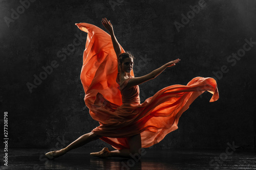 Fototapeta Naklejka Na Ścianę i Meble -  Ballerina. Silhouette photo of a young  ballet dancer dressed in a long peach dress, pointe shoes with ribbons. The girl performs an graceful dance movement. Beautiful classic ballet. Ballet studios.