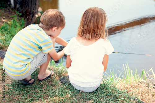 Children fishing on the bank of the river. Two friends catching a fish during a hot summer day. View from the back.