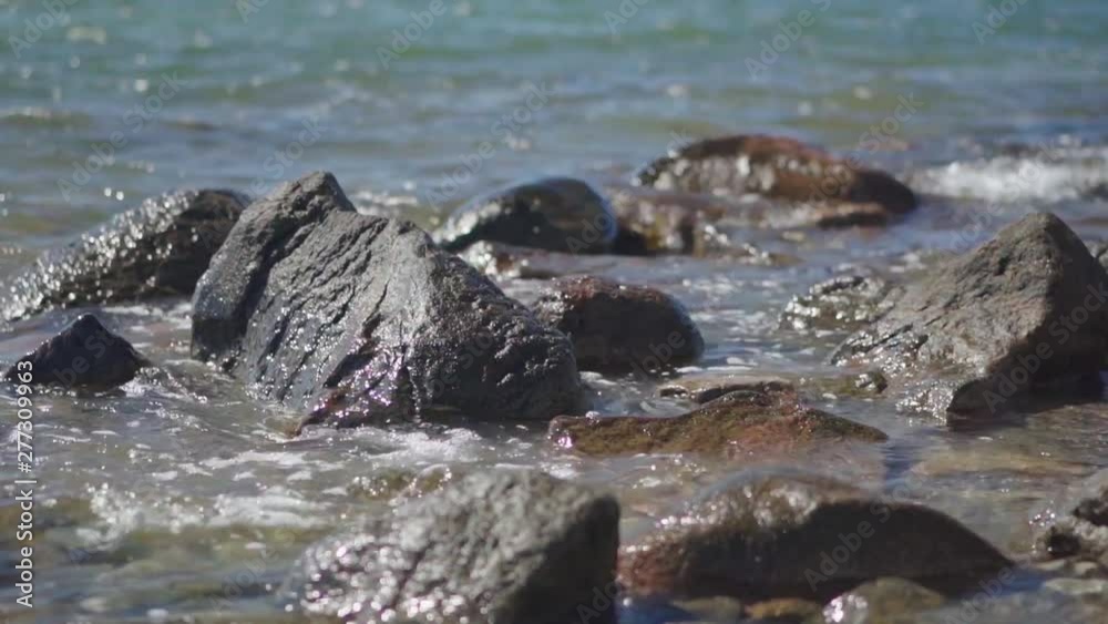 Slow Motion, waves splashing over rocks and wash around them on a sunny day Slow Motion, waves splashing over rocks and wash around them on a sunny day