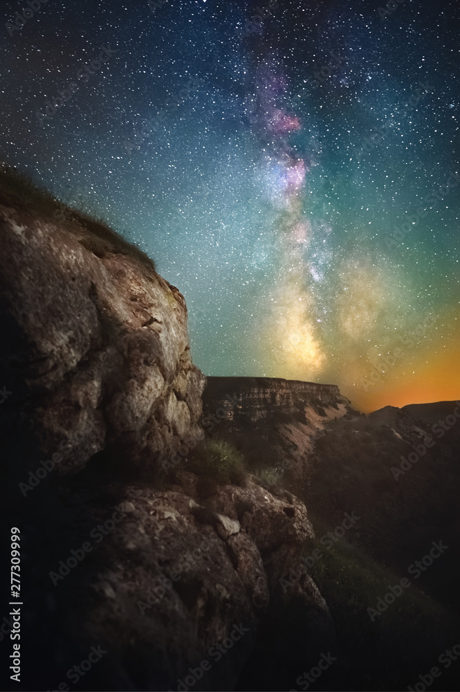 Night landscape of a cliff with a gorge in the background and a vertical Milky Way. Dreamy image in a fabulous way