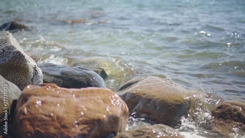 Slow Motion, waves splashing over rocks and wash around them on a sunny day