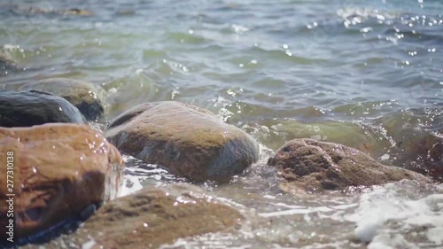 Slow Motion, waves splashing over rocks and wash around them on a sunny day
