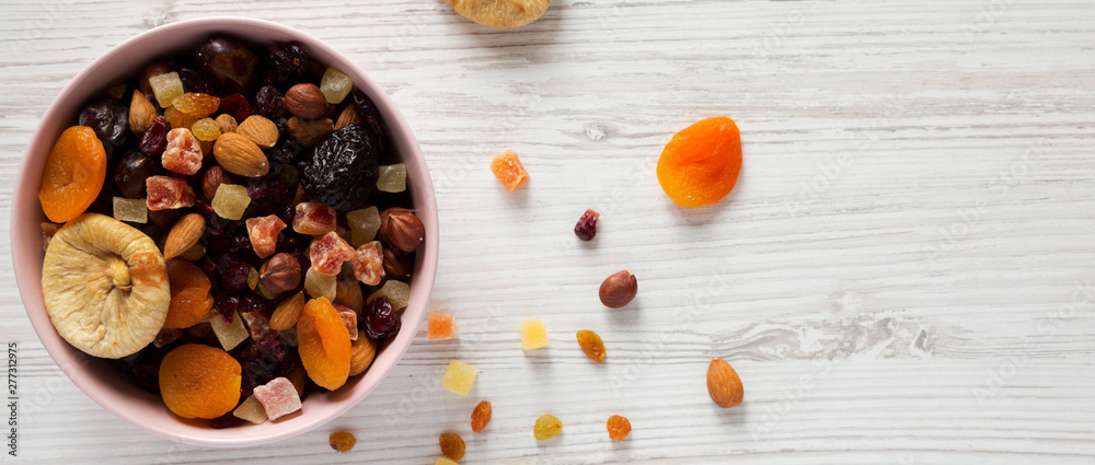 Full pink bowl of dried fruits and nuts on a white wooden surface, top view. Overhead, from above, flat lay. Space for text. Full pink bowl of dried fruits and nuts on a white wooden surface, top view. Overhead, from above, flat lay. Space for text.