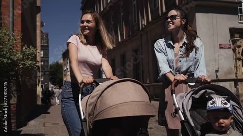 young happy mothers women with baby strollers walk down the street talking walk