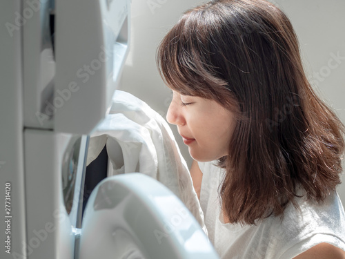 Beautiful Asian woman smelling white clean linen shirt after washing from washing machine