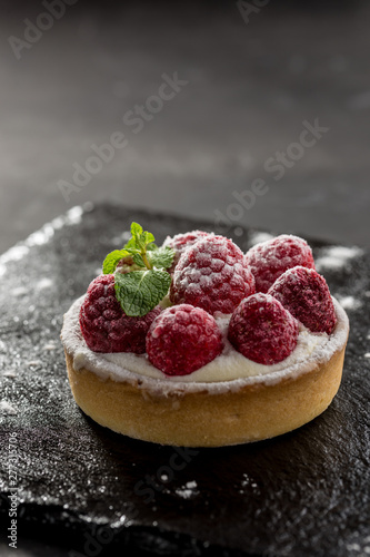 Raspberry tartlets with icing sugar close up on stone board on black background